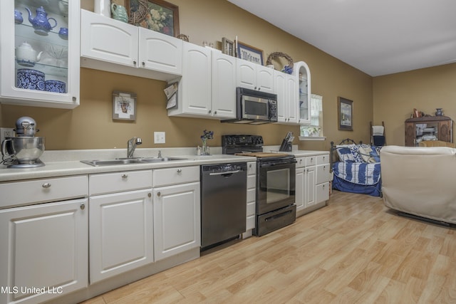 kitchen with white cabinets, a sink, light countertops, light wood-style flooring, and black appliances