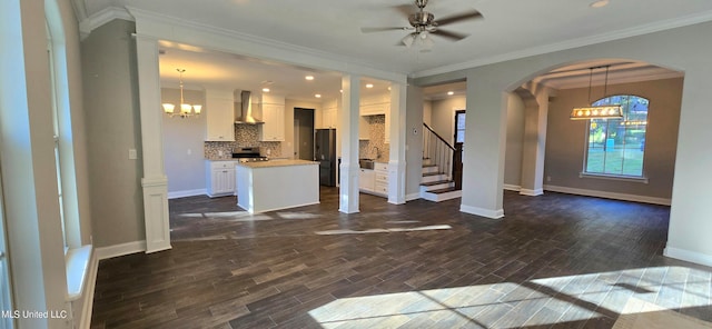 unfurnished living room featuring ornamental molding, dark wood-type flooring, and ceiling fan with notable chandelier