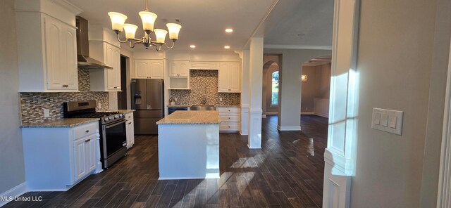 kitchen with wall chimney range hood, appliances with stainless steel finishes, a center island, hanging light fixtures, and dark wood-type flooring