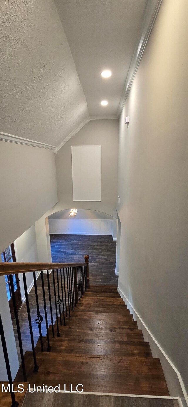 stairs with crown molding, hardwood / wood-style floors, a textured ceiling, and lofted ceiling