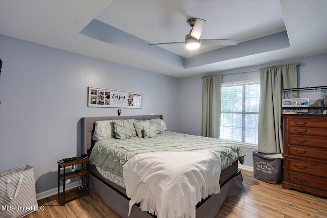 bedroom with ceiling fan, wood-type flooring, and a tray ceiling