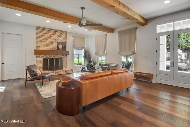 living room with beamed ceiling, ceiling fan, a brick fireplace, and dark hardwood / wood-style flooring