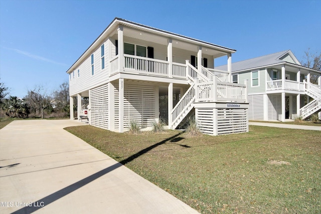 raised beach house with covered porch, stairs, concrete driveway, a carport, and a front lawn