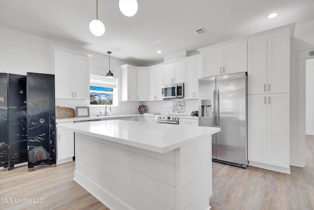 kitchen with visible vents, a center island, stainless steel appliances, white cabinets, and light wood finished floors