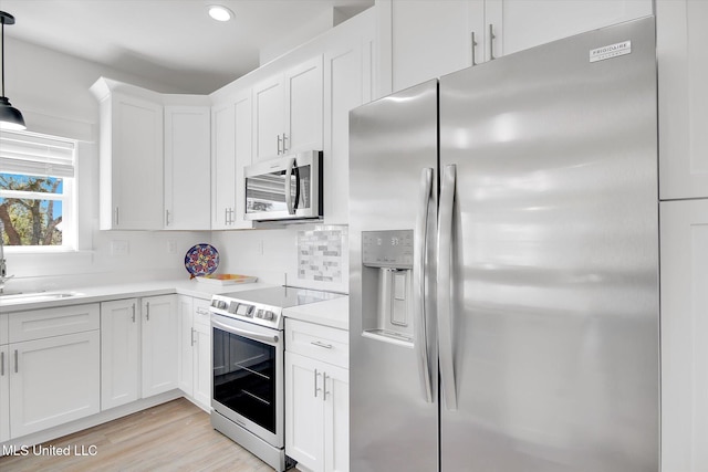 kitchen with stainless steel appliances, white cabinets, light wood finished floors, decorative backsplash, and light countertops