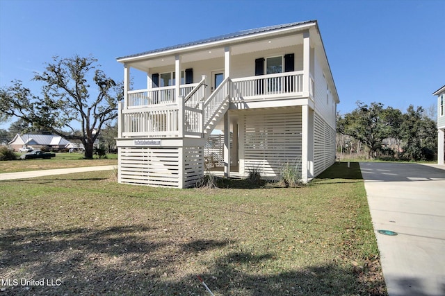 beach home with metal roof, a porch, concrete driveway, and a front lawn