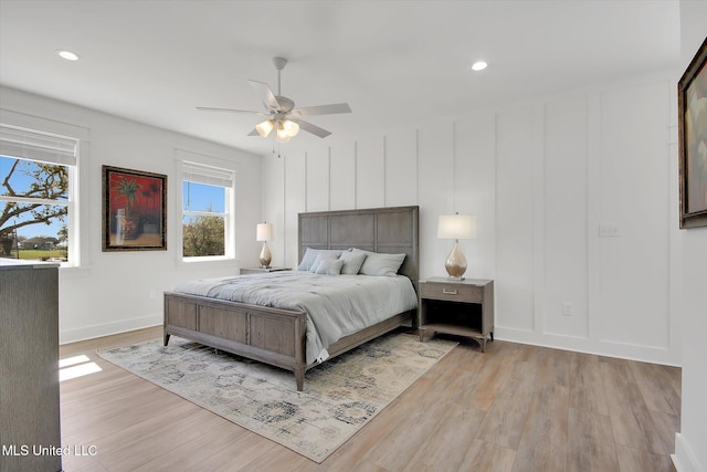 bedroom with a ceiling fan, recessed lighting, light wood-style floors, a decorative wall, and baseboards