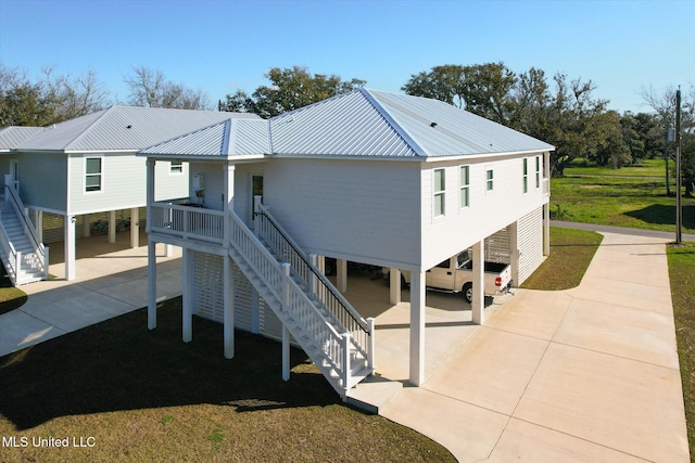 rear view of property featuring a lawn, driveway, metal roof, a carport, and stairs