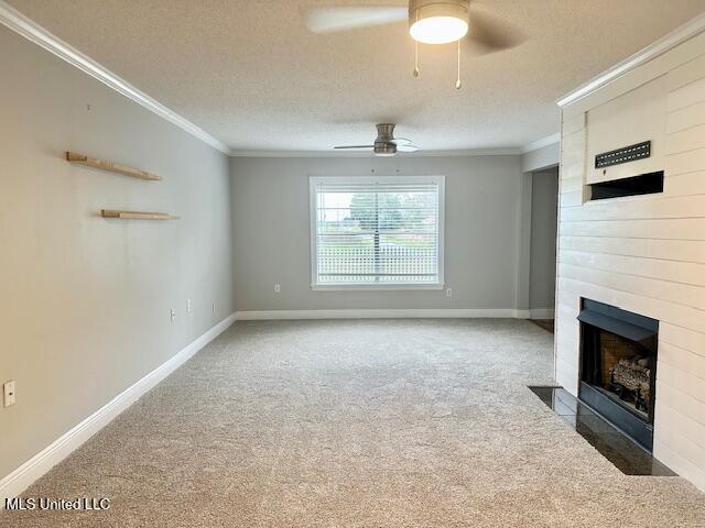 unfurnished living room featuring ceiling fan, a large fireplace, carpet floors, a textured ceiling, and ornamental molding