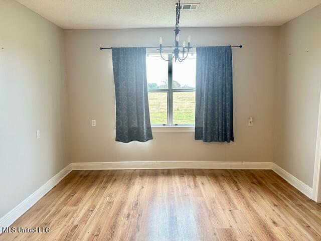 unfurnished room featuring a textured ceiling, a notable chandelier, and light wood-type flooring