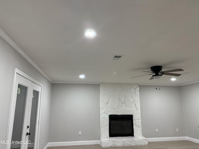 unfurnished living room with hardwood / wood-style flooring, ornamental molding, a stone fireplace, and ceiling fan