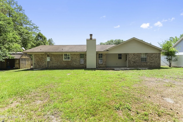 back of house featuring a chimney, brick siding, a storage unit, a lawn, and an outbuilding