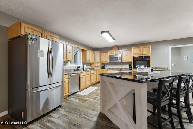 kitchen featuring appliances with stainless steel finishes, a textured ceiling, hardwood / wood-style flooring, a center island, and a breakfast bar area