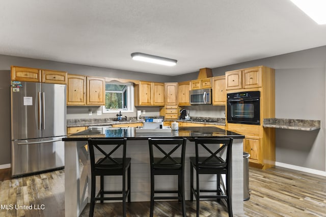 kitchen with a breakfast bar, sink, black appliances, wood-type flooring, and a center island