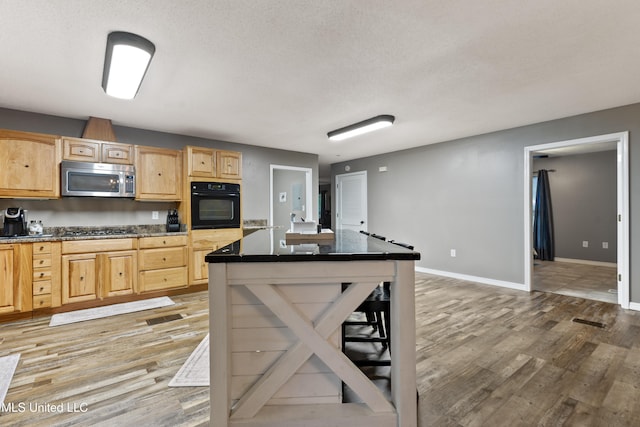 kitchen featuring appliances with stainless steel finishes, light brown cabinetry, a textured ceiling, hardwood / wood-style floors, and a kitchen island