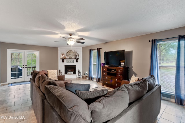 tiled living room featuring french doors, a textured ceiling, a large fireplace, and ceiling fan