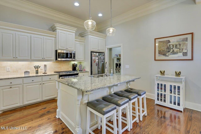 kitchen with stainless steel appliances, a sink, a kitchen breakfast bar, ornamental molding, and decorative backsplash