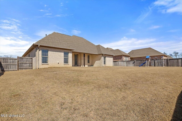 rear view of house with a playground, a fenced backyard, brick siding, roof with shingles, and a lawn