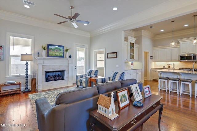 living room featuring a tiled fireplace, visible vents, crown molding, and hardwood / wood-style floors