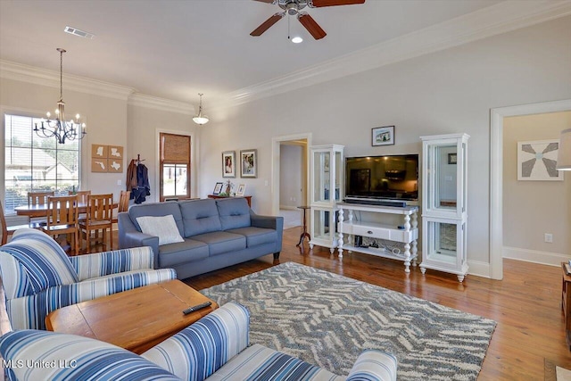 living room with ceiling fan with notable chandelier, wood finished floors, visible vents, baseboards, and ornamental molding