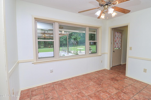 empty room featuring ceiling fan, light stone finish flooring, baseboards, and wainscoting