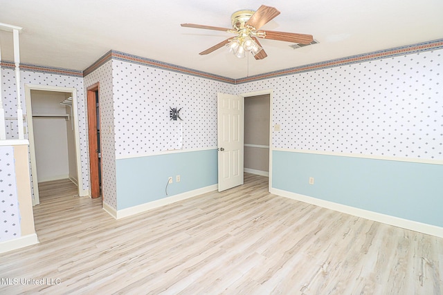 unfurnished bedroom featuring crown molding, wood finished floors, baseboards, wallpapered walls, and ceiling fan