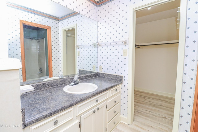 full bathroom featuring wood finished floors, baseboards, a shower, vanity, and wallpapered walls