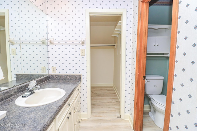 bathroom featuring wood finished floors, baseboards, vanity, and toilet