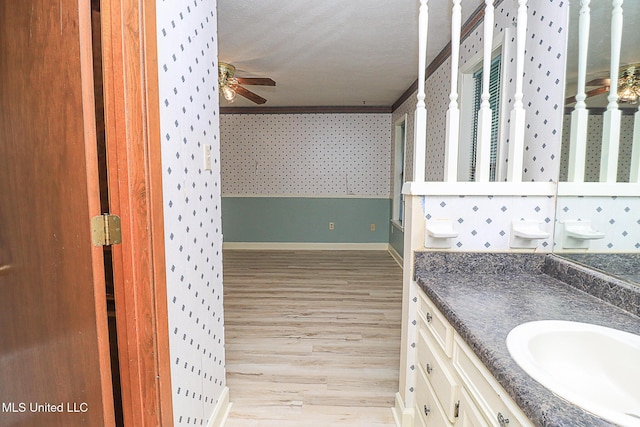 bathroom featuring wood finished floors, a ceiling fan, baseboards, vanity, and wallpapered walls