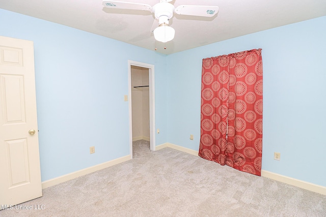 unfurnished bedroom featuring carpet floors, a spacious closet, baseboards, and ceiling fan