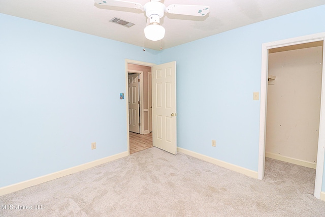 unfurnished bedroom featuring carpet flooring, a walk in closet, baseboards, a ceiling fan, and a closet