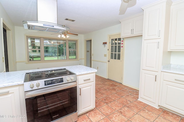 kitchen featuring electric range, ceiling fan, island exhaust hood, white cabinetry, and wainscoting