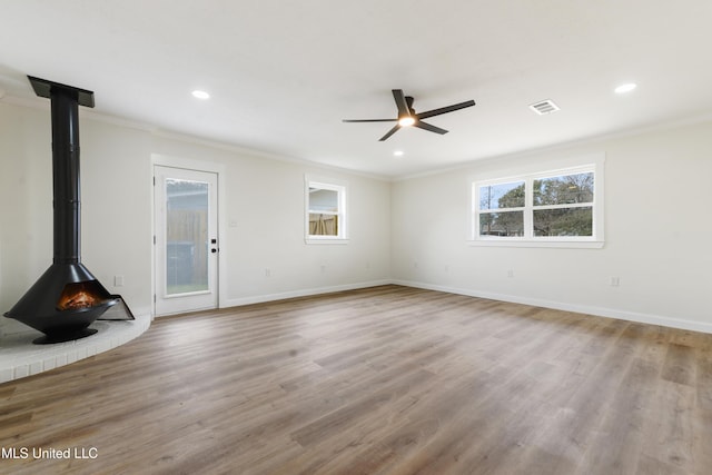 unfurnished living room with a wood stove, baseboards, ornamental molding, and wood finished floors