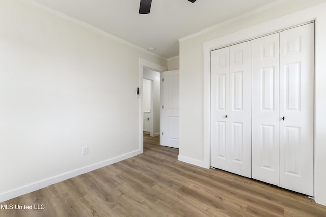 unfurnished bedroom with a closet, ornamental molding, ceiling fan, wood finished floors, and baseboards