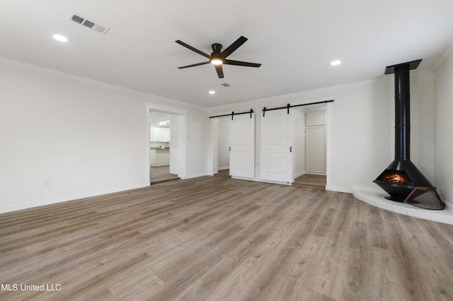 unfurnished living room featuring crown molding, visible vents, a barn door, ceiling fan, and light wood-type flooring