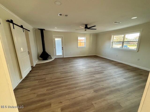 empty room featuring a barn door, wood finished floors, visible vents, and baseboards