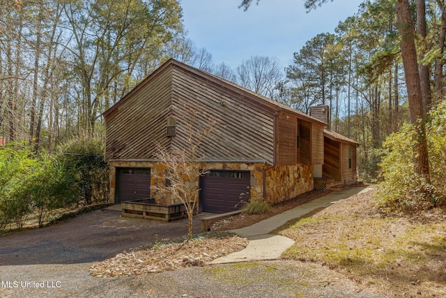 view of home's exterior featuring aphalt driveway, stone siding, a chimney, and an attached garage