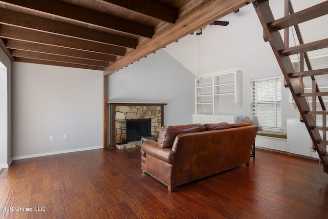 living room featuring lofted ceiling with beams, a stone fireplace, wood finished floors, baseboards, and stairway