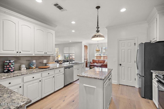 kitchen with white cabinets, appliances with stainless steel finishes, a kitchen island, backsplash, and hanging light fixtures