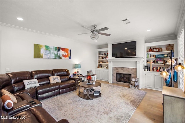 living room featuring ceiling fan, a brick fireplace, crown molding, light hardwood / wood-style flooring, and built in shelves