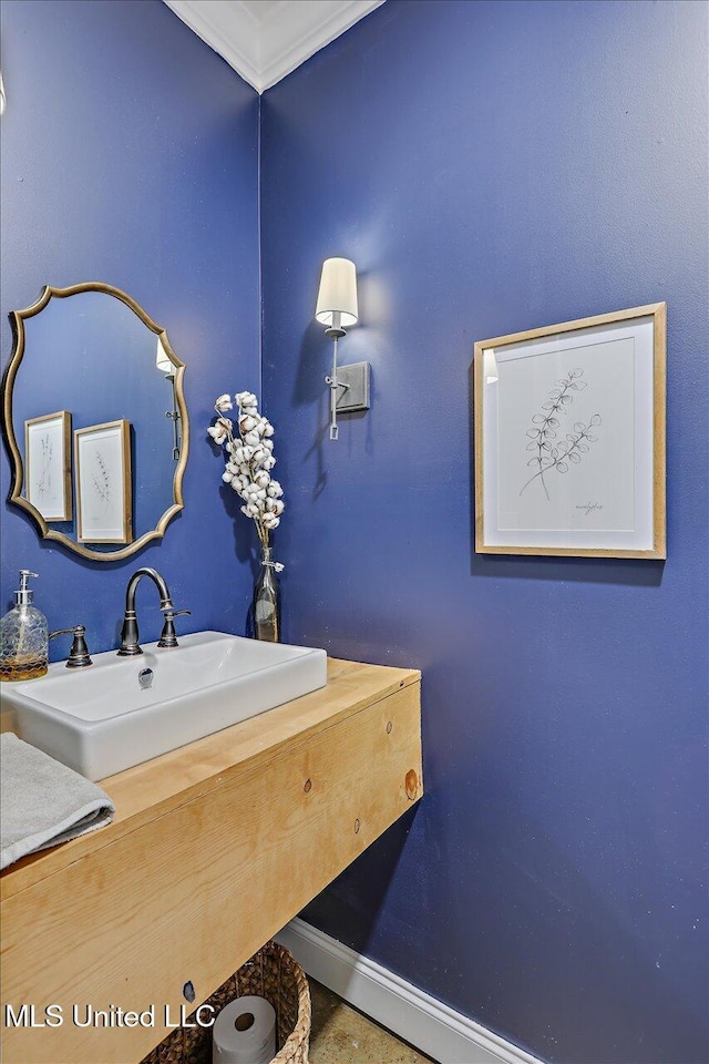 bathroom featuring crown molding, a sink, and baseboards