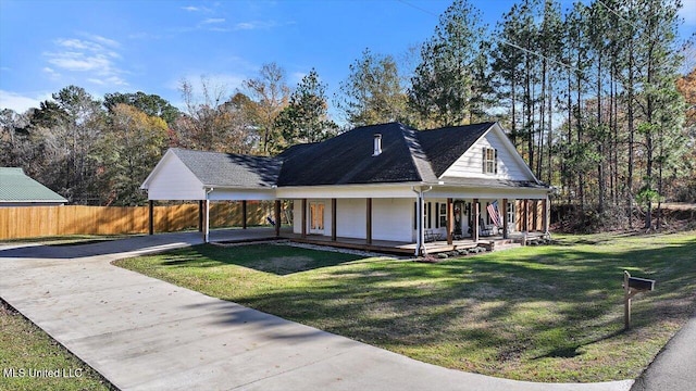 farmhouse-style home with driveway, covered porch, fence, and a front yard