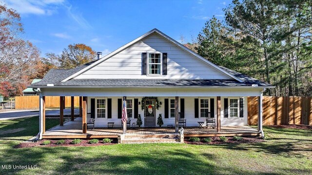 rear view of property with a shingled roof, fence, a porch, and a yard