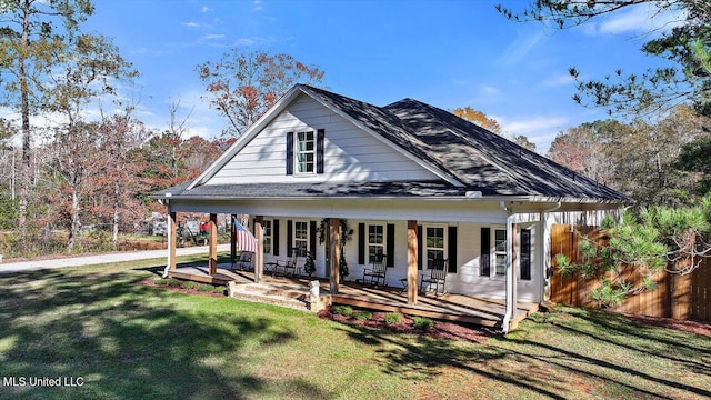 farmhouse-style home featuring covered porch, a shingled roof, fence, and a front lawn