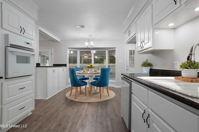 kitchen with stainless steel dishwasher, white cabinetry, hardwood / wood-style flooring, and oven