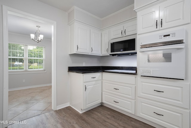 kitchen with white oven, white cabinetry, crown molding, a notable chandelier, and light hardwood / wood-style flooring