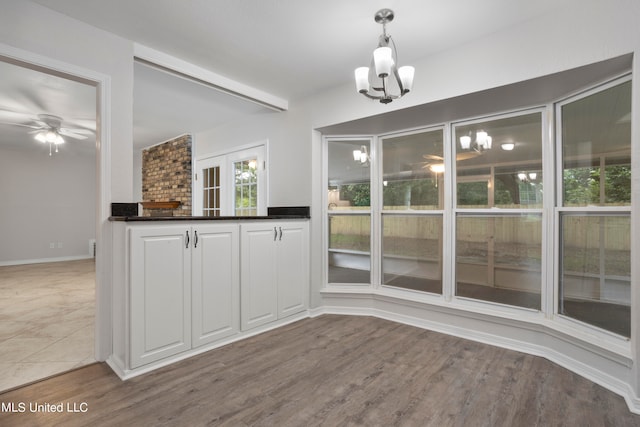 unfurnished dining area with wood-type flooring, a brick fireplace, and ceiling fan with notable chandelier