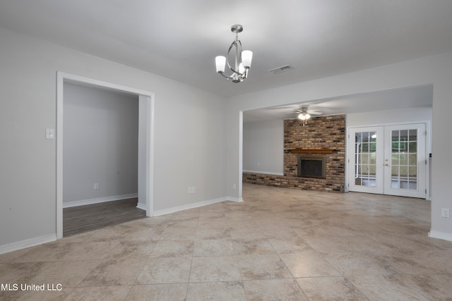 unfurnished living room featuring french doors, ceiling fan with notable chandelier, and a brick fireplace