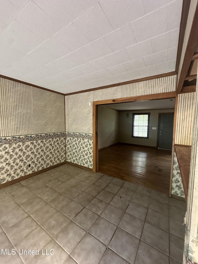 tiled empty room featuring wallpapered walls, baseboards, and crown molding