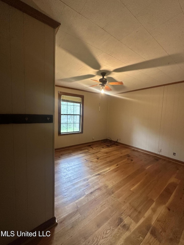 empty room featuring wood-type flooring, a ceiling fan, and baseboards